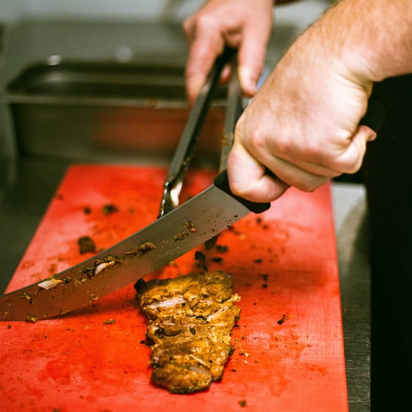 Chef's hands slicing seasoned meat on a red cutting board for Hey Juan Burritos.