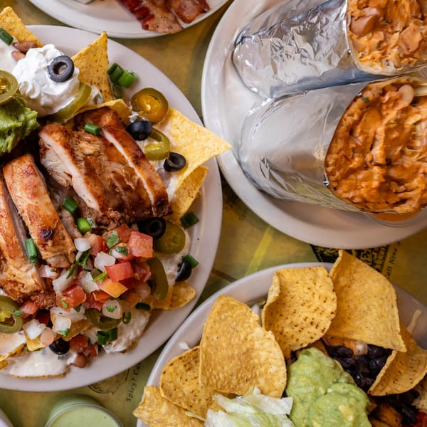 Plates of chicken nachos, burritos, and a taco salad with guacamole and black beans.