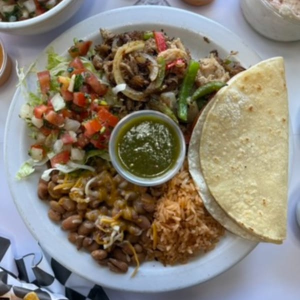 A plate of fajitas with steak, onions, peppers, rice, beans, salsa, and tortillas.