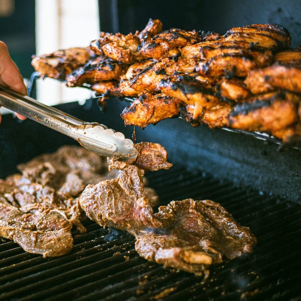 Marinated chicken and beef cooking on a grill, with tongs turning the meat.