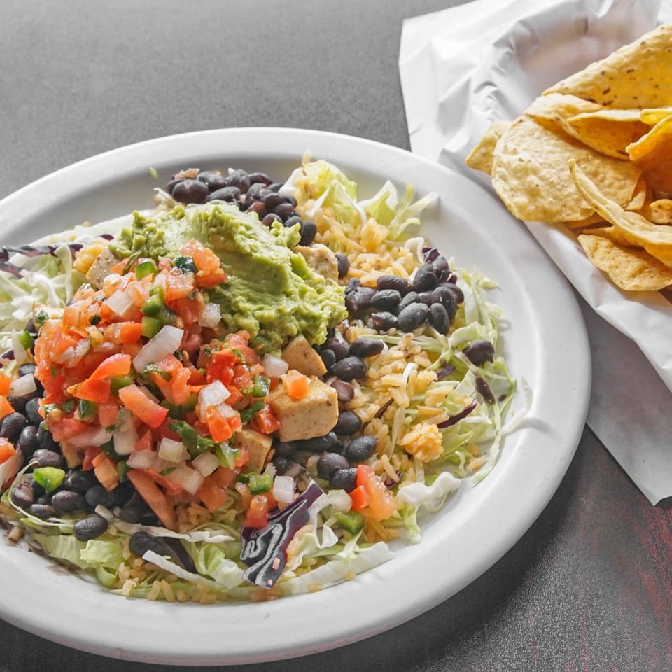 Mexican-inspired salad bowl topped with guacamole, pico de gallo, black beans, rice, lettuce, and tortilla chips.