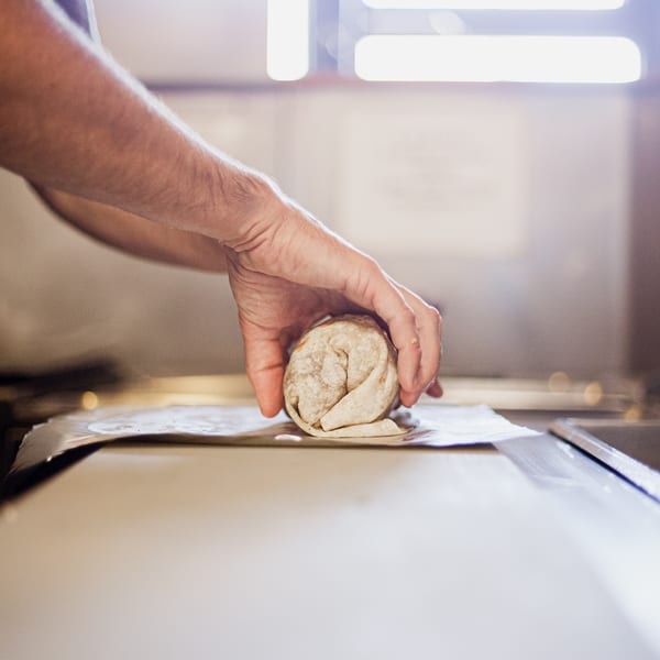 Hands carefully rolling a large burrito in a tortilla on a piece of parchment paper.