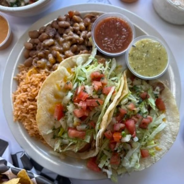 Two tacos with lettuce and tomatoes, served with rice, beans, red salsa, and green salsa.