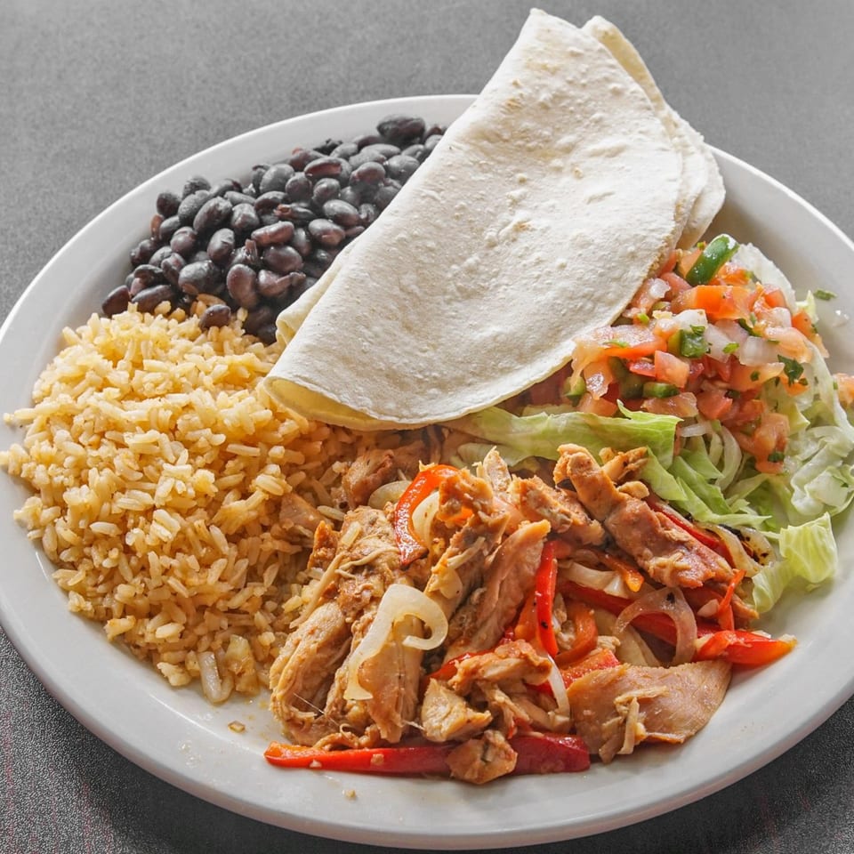 Mexican plate with a flour tortilla, seasoned rice, black beans, shredded chicken with peppers, lettuce, and pico de gallo.