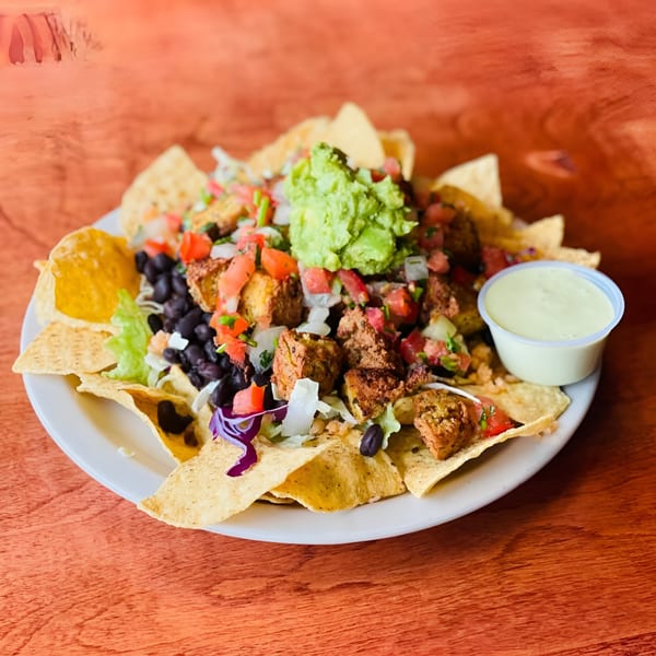 A plate of Hey Juan Burritos nachos with black beans, pico de gallo, guacamole, and a side of sauce.