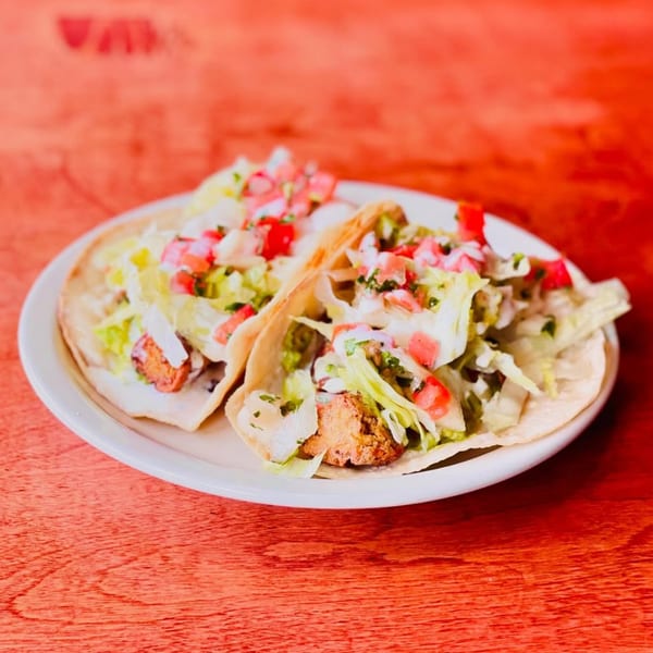 Two Hey Juan Burritos tacos filled with meat, lettuce, pico de gallo, and crema on a white plate.