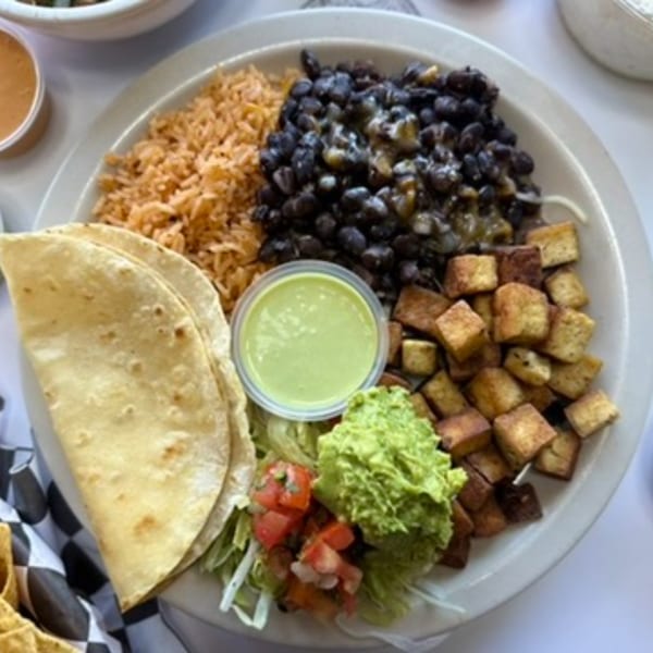 A plate of Mexican food with rice, black beans, fried tofu, guacamole, salsa, and tortillas.