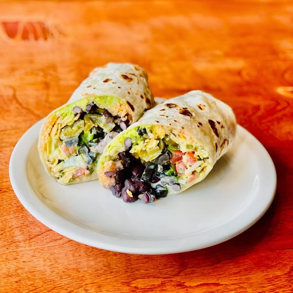 Two Hey Juan Burritos, cut in half, revealing black beans, rice, lettuce, and cheese on a white plate.