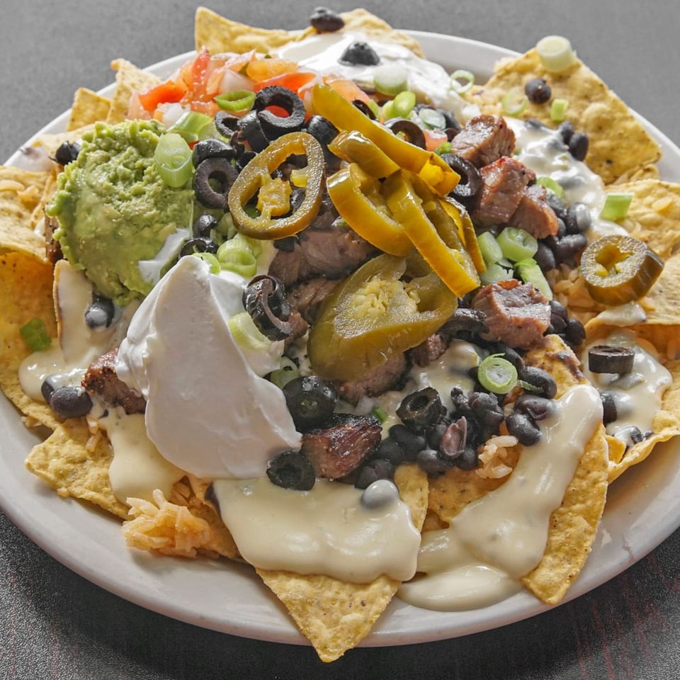Loaded nachos topped with grilled steak, melted cheese, guacamole, sour cream, black beans, olives, jalapeños, and vegetables.