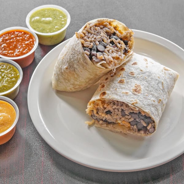 Two cut burritos filled with rice, black beans, and vegetables sit on a plate beside cups of colorful salsa.