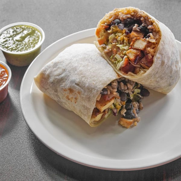 Two stuffed burritos filled with rice, black beans, vegetables, and grilled tofu sit on a plate with dipping sauces.