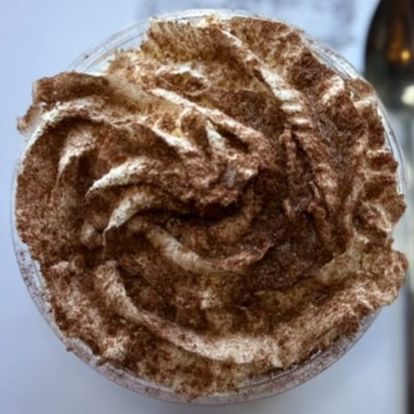 Close-up overhead view of a dessert cup filled with whipped cream and dusted with cocoa powder.